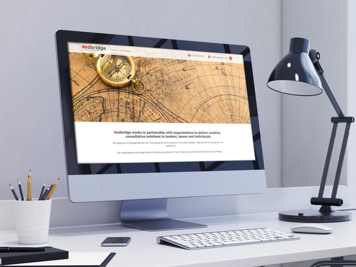 A website design shown on a desktop computer on a desk with a lamp next to it